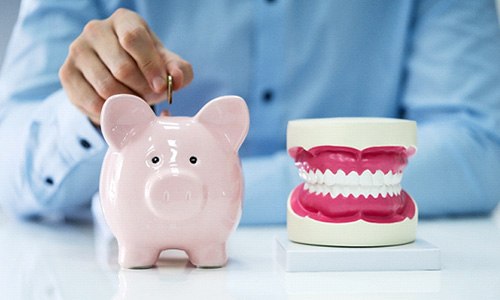 A man placing a coin in a piggy bank that’s next to a model jaw