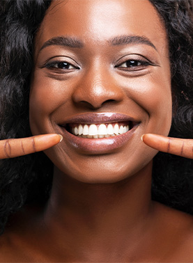 Young woman with white teeth pointing to her smile