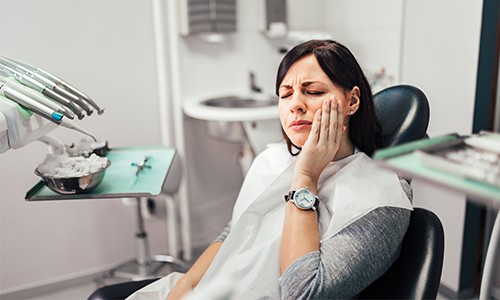 Woman in dental chair holding cheek