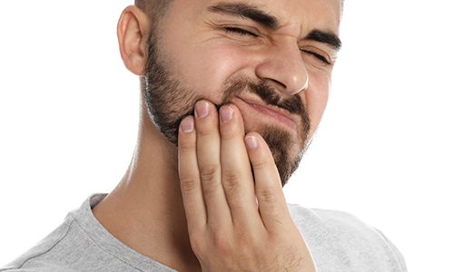 A younger man with a beard cringing in pain and holding his jaw area