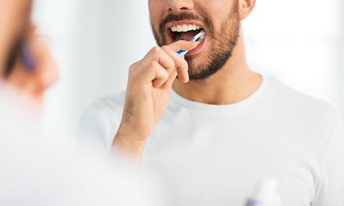 Man smiling while brushing his teeth in bathroom