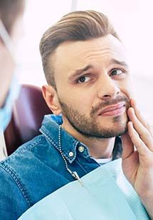 Man in dental chair holding his cheek in pain