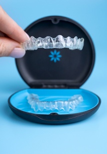 Fingers lifting Invisalign from its case with blue background