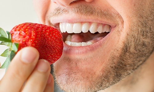 Closeup of patient eating strawberry to prevent dental emergencies in Big Pine Key