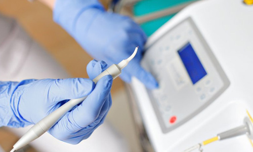 Dentist holding a dental laser while pushing a button on the machine