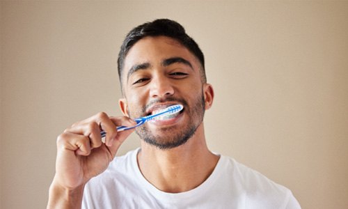 Man in white shirt smiling while brushing his teeth