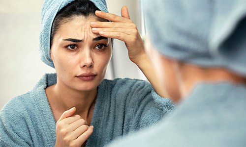 Woman looking at herself in mirror, concerned about forehead wrinkles