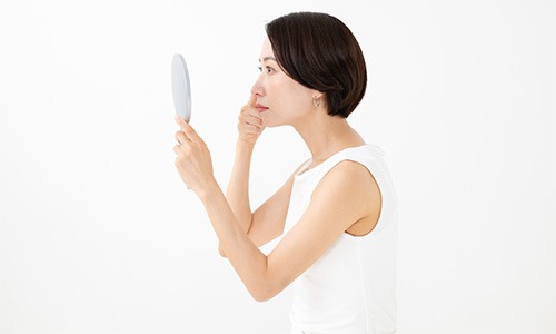 Woman looking in mirror, concerned about signs aging