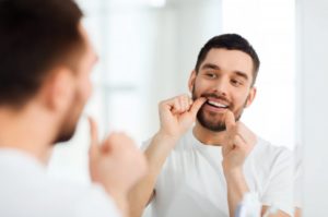 bearded man in white shirt flossing