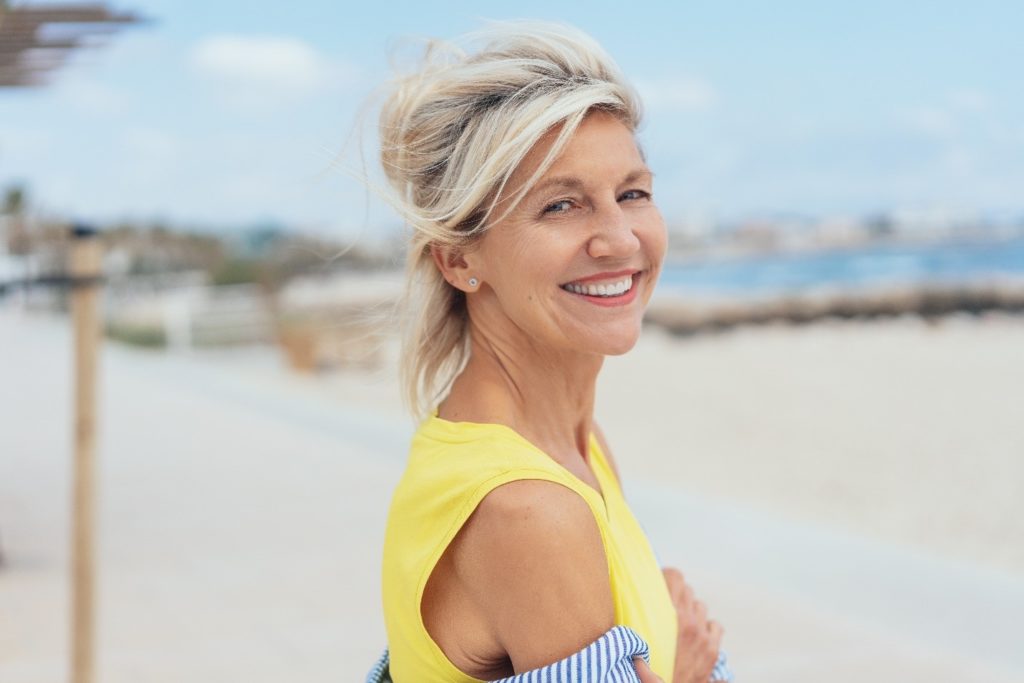 Woman with dental implants on the beach during the summertime.