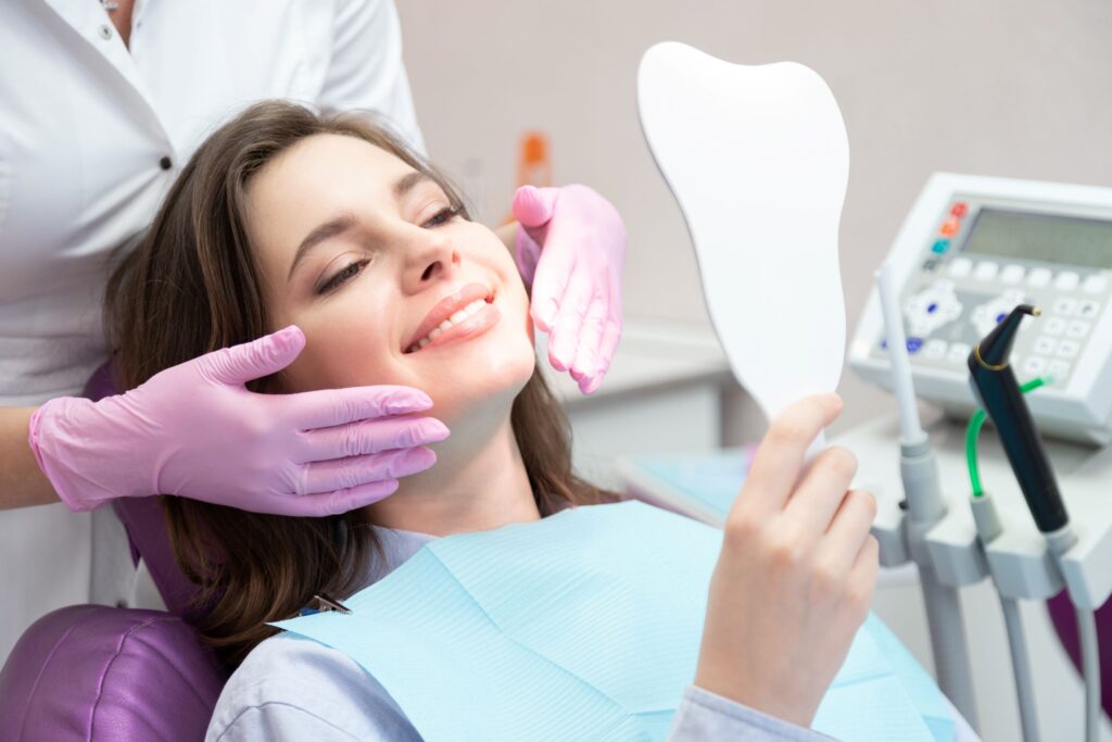Dentist in purple gloves touching patient's cheeks as she smiles in mirror
