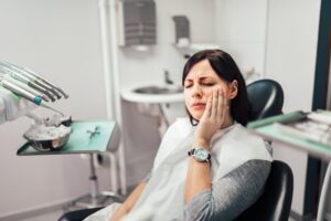 Woman in dentist's chair holding face in pain. 