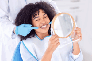 Woman in the patient’s chair smiling in a handheld mirror