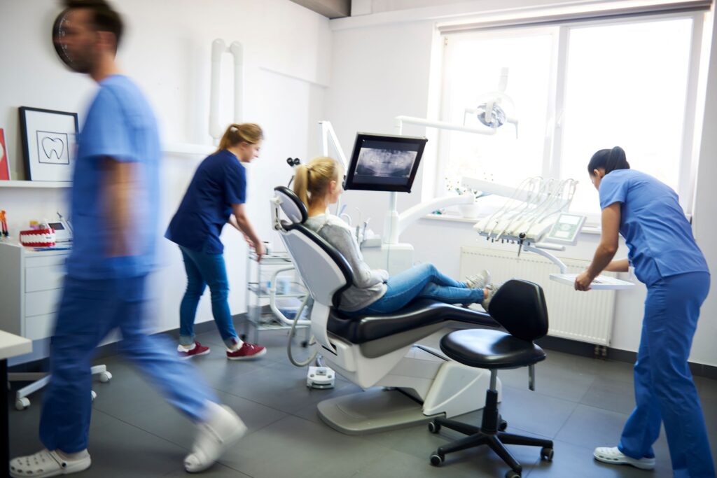 Woman in dental chair with 3 people in scrubs blurry in motion