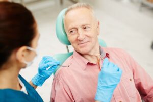 Older man in dentist's chair looking at hygienist. 