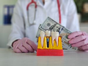 Dentist's gloved hands holding $100 bills behind model dental implant